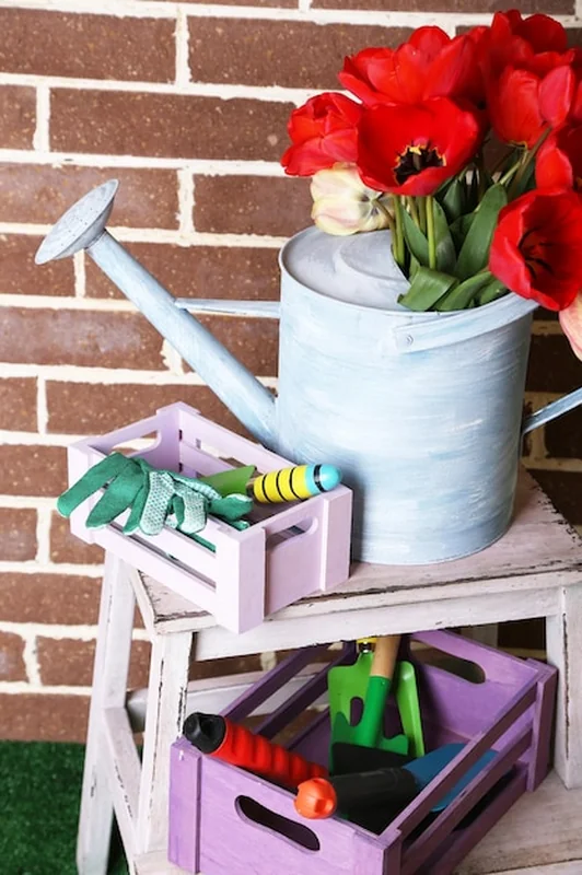 Kompozycja kolorowych tulipanów w konewce i sprzęt ogrodniczy na jasnym tle