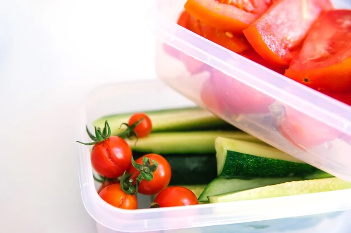 Plasterki warzyw w pojemnikach na białym tle: ogórki i pomidory