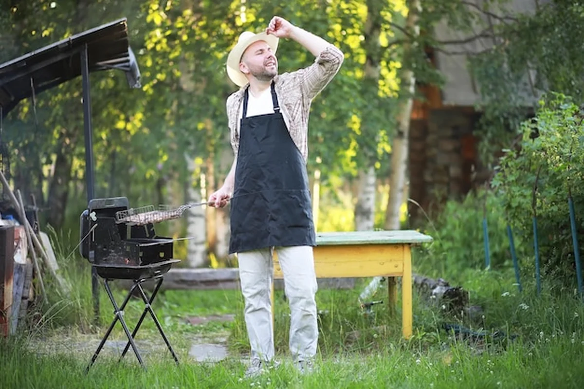 Europejczyk w kapeluszu czeka na jedzenie z grilla, siedząc w pobliżu ognia