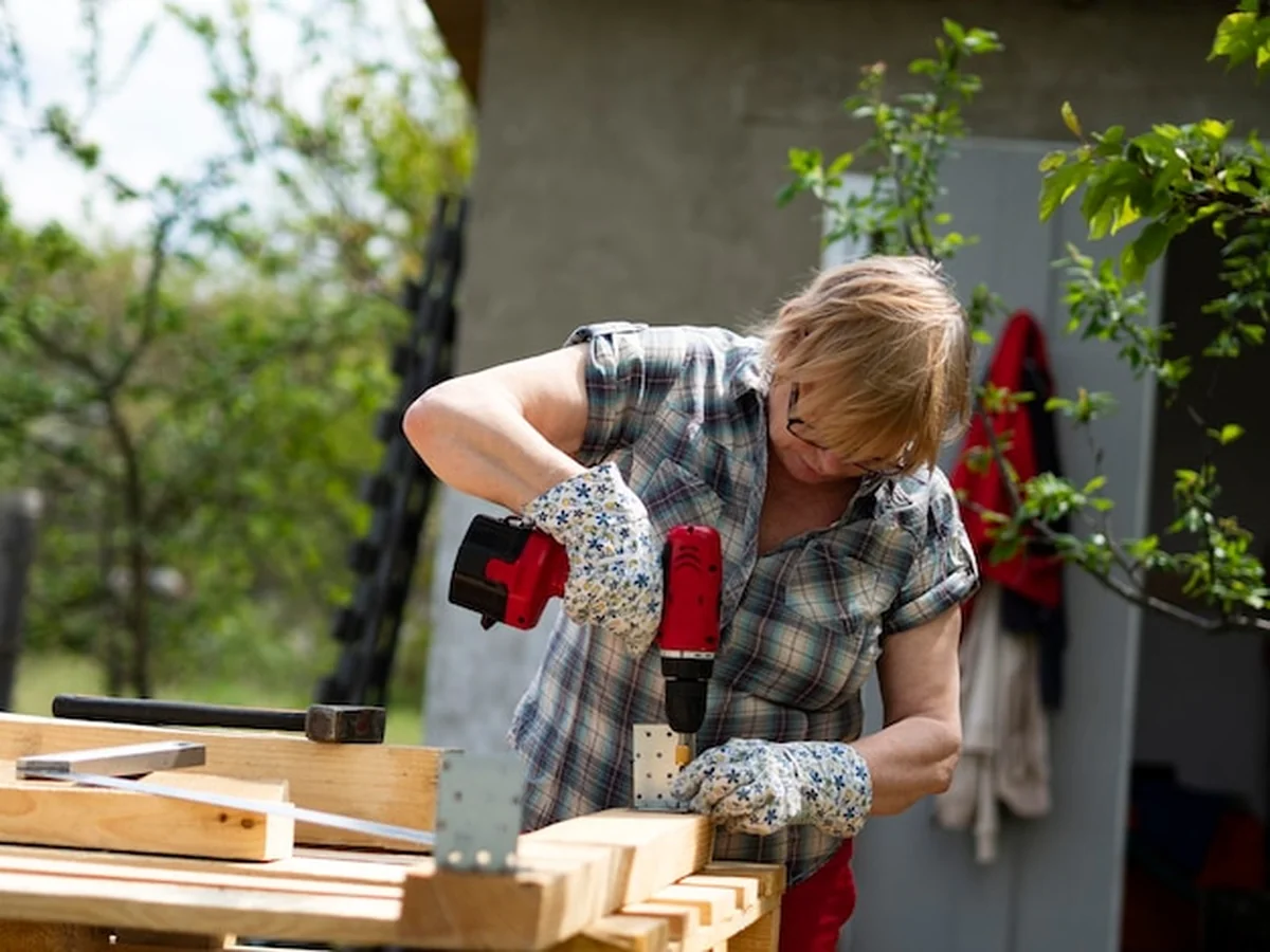 Starsza kobieta kaukazyjska montuje drewnianą ramę budynku za pomocą metalowych przymoców