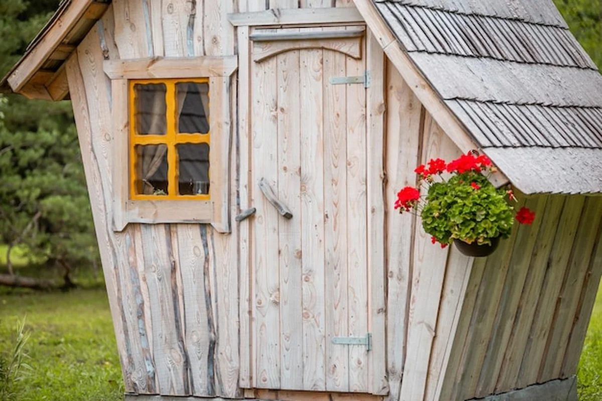Rustyczna drewniana chatka z żółtym oknem i czerwonym garnkiem
