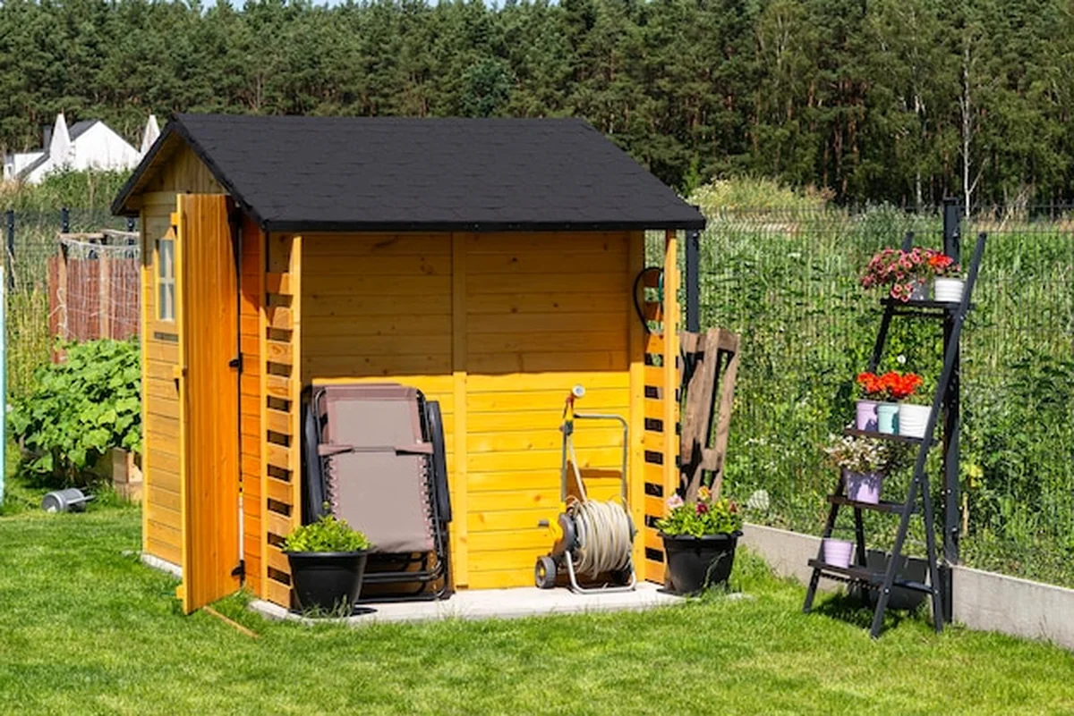 Drewniana szopa ogrodowa na betonowym fundamencie z kwiatami i narzędziami