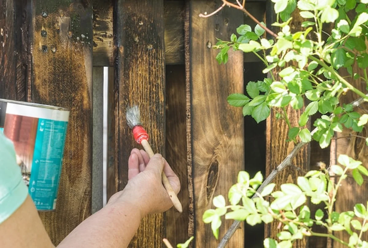 Kobieta maluje drewniany taras pędzlem