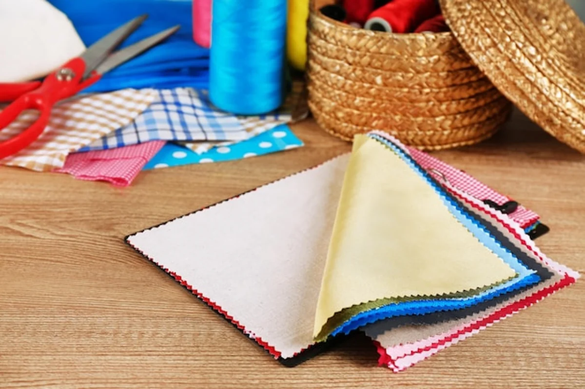 Kolorowe próbki tkanin i koszyk z nitkami na drewnianym tle stołu