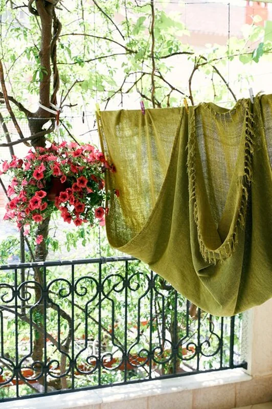 Na balkonie wiszą zielony koc i doniczka z czerwonymi kwiatami